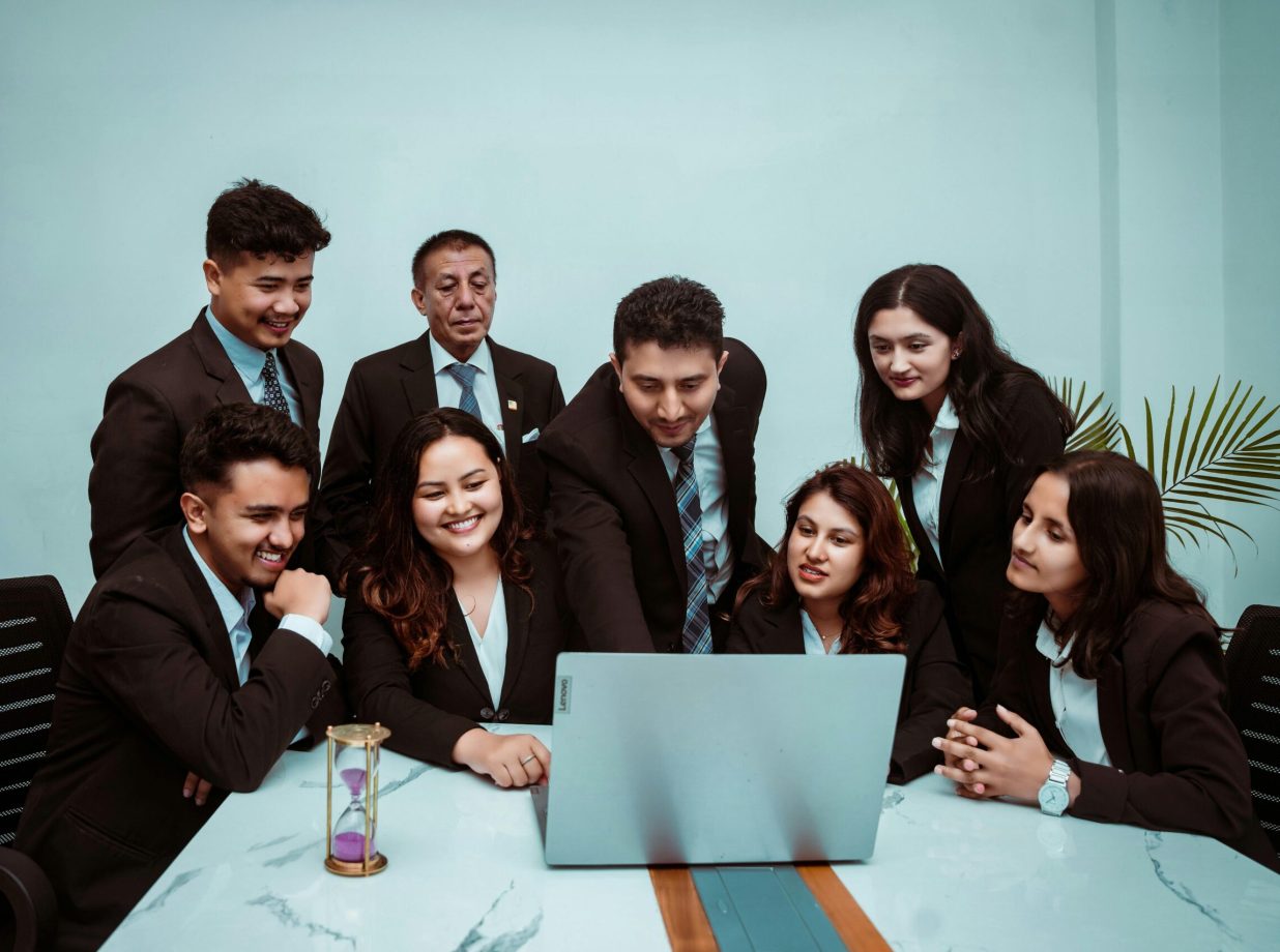A diverse team of professionals collaborating around a laptop in a modern office setting.